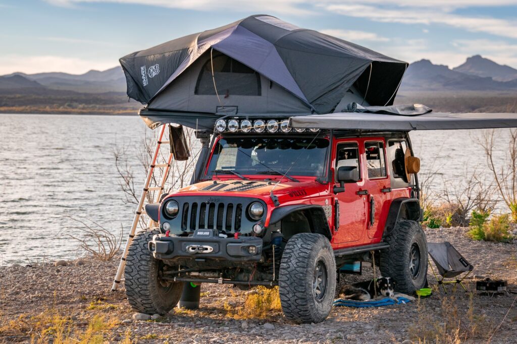 Clifford with its rooftop tent at a lakeside camp at sunset