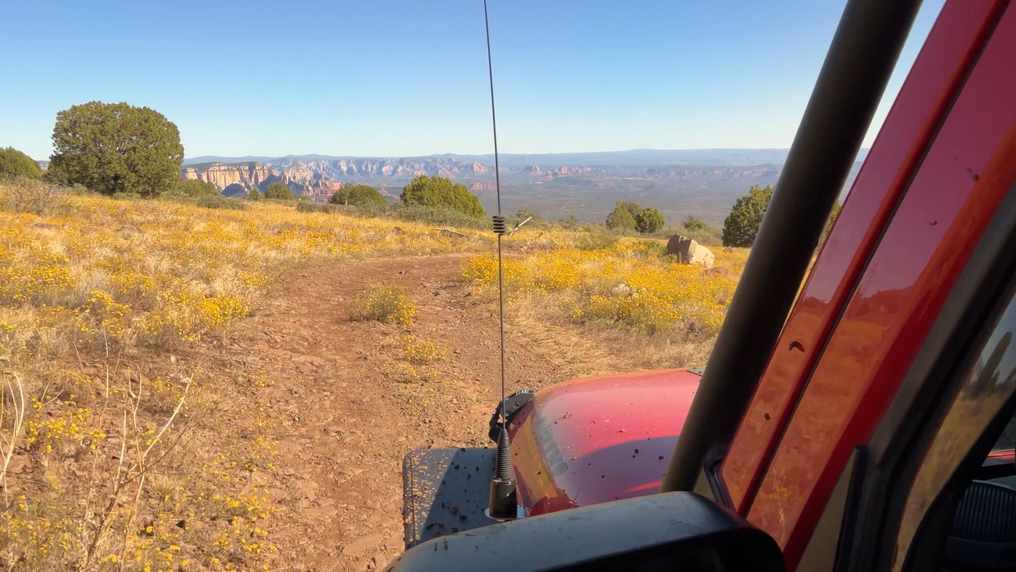 Yellow grass and red rock formations ahead from inside a Jeep