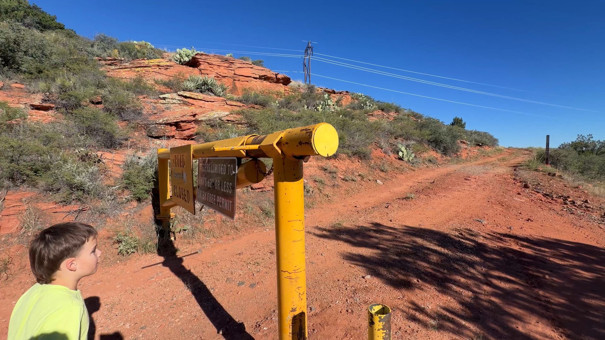 A boy next to a yellow Forest Service gate on red dirt