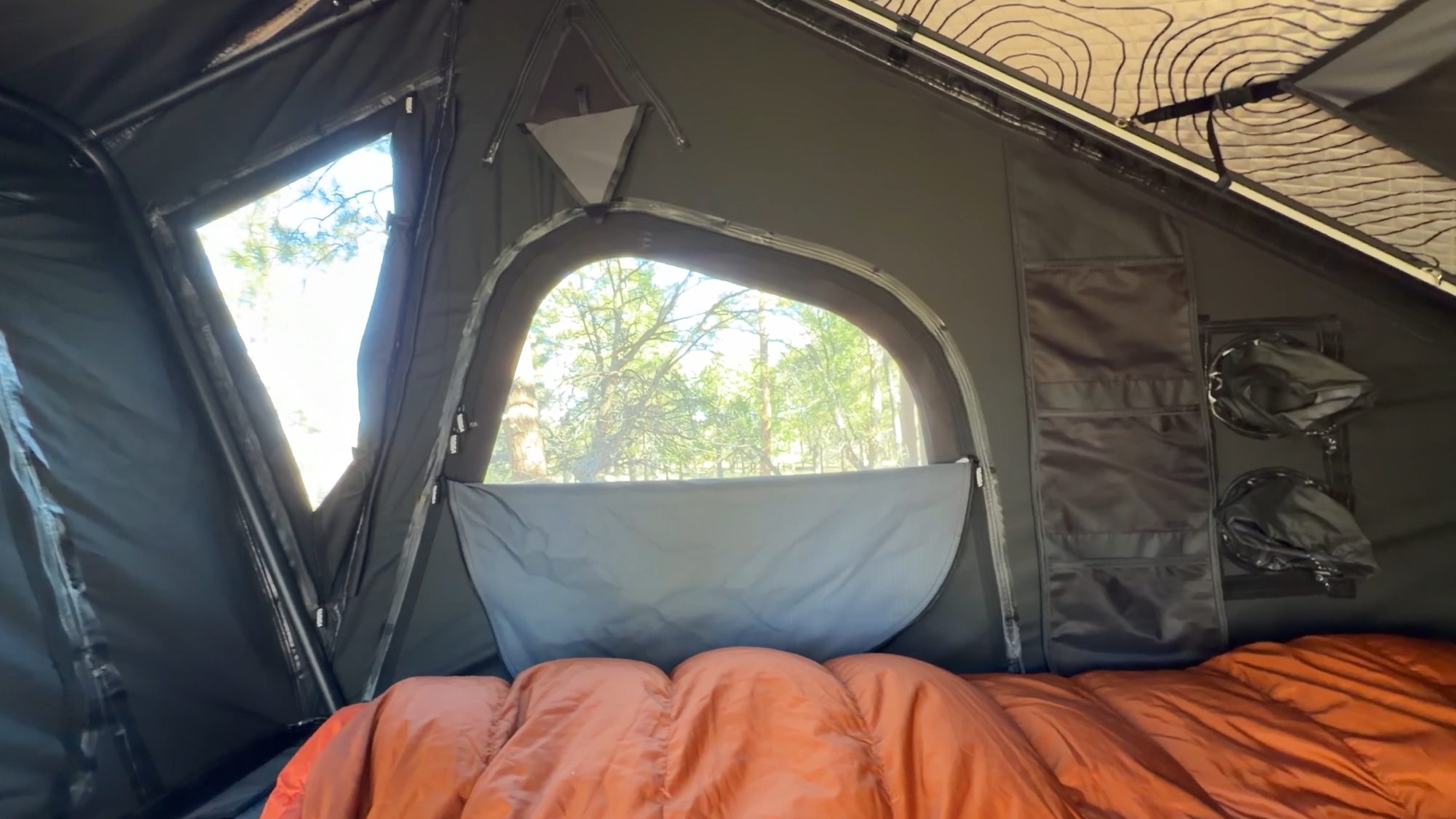 Inside a rooftop tent with windows and an orange sleeping bag