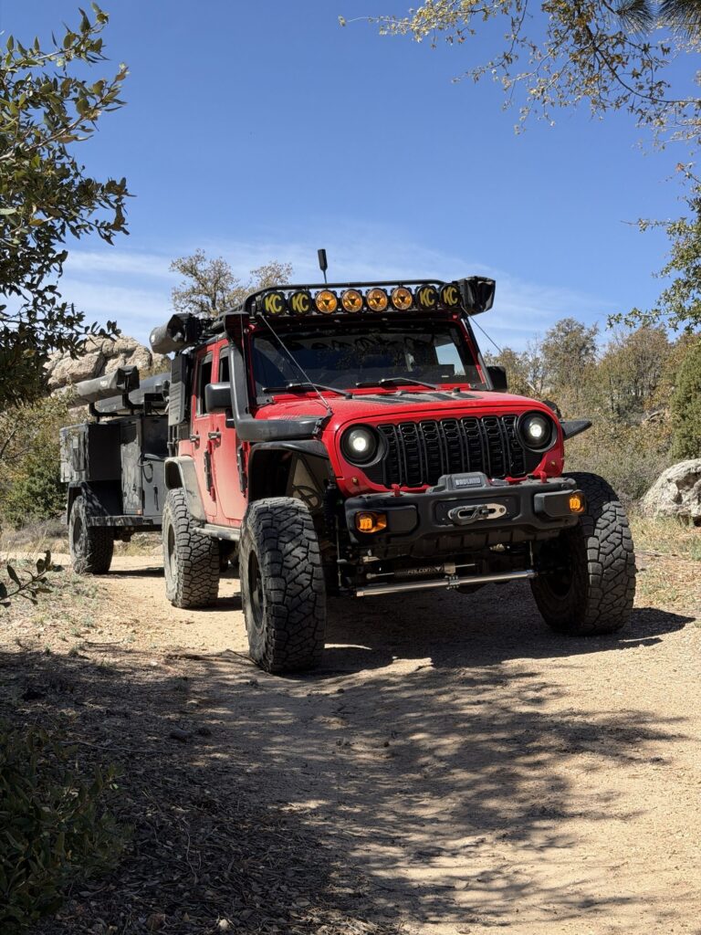 Red Jeep Wrangler towing a Turtleback off-road trailer on a dirt road in the Bradshaw Mountains