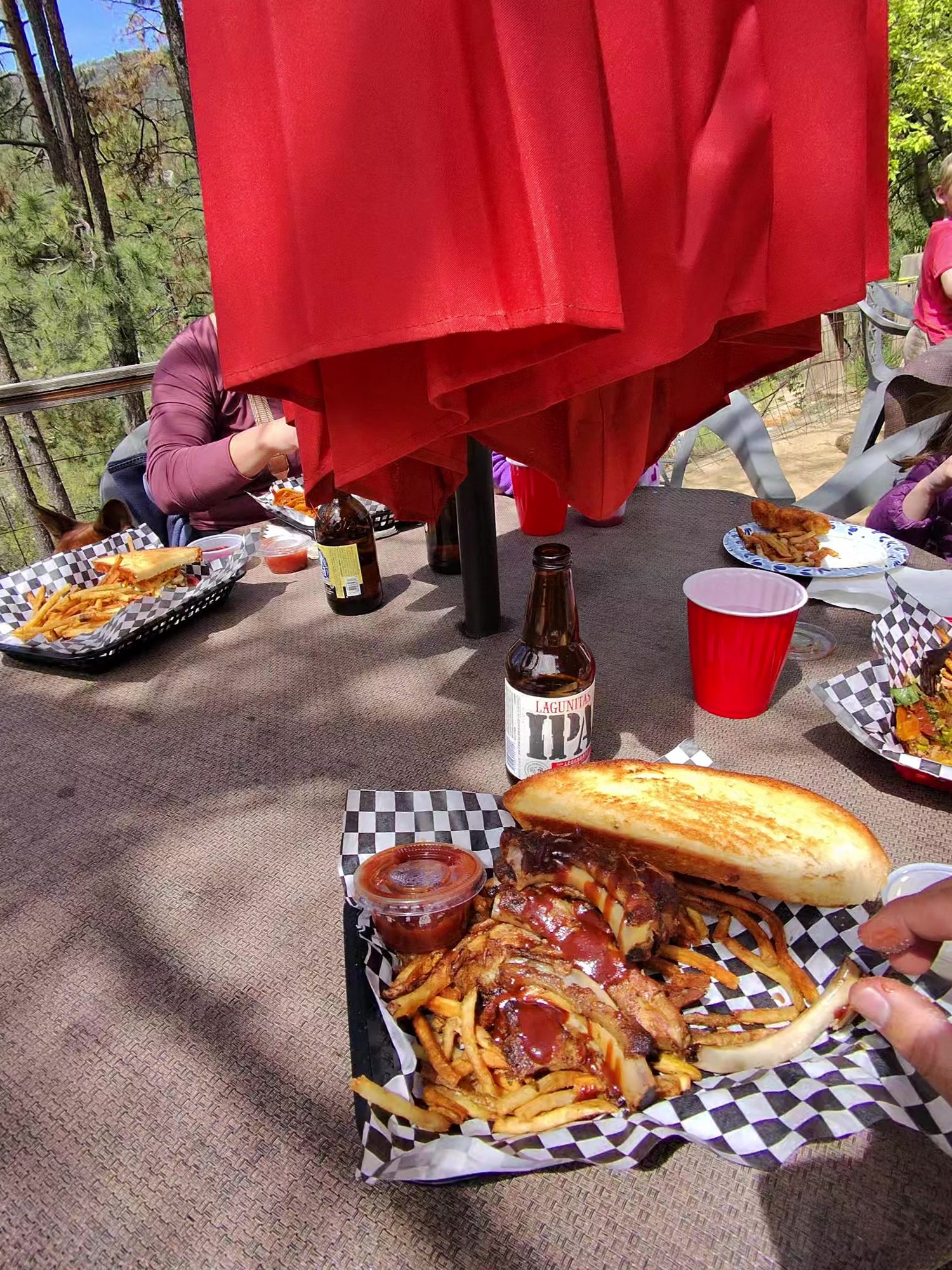 Barbecue sandwich and fries in a checkered basket on The Mill’s patio under red umbrellas