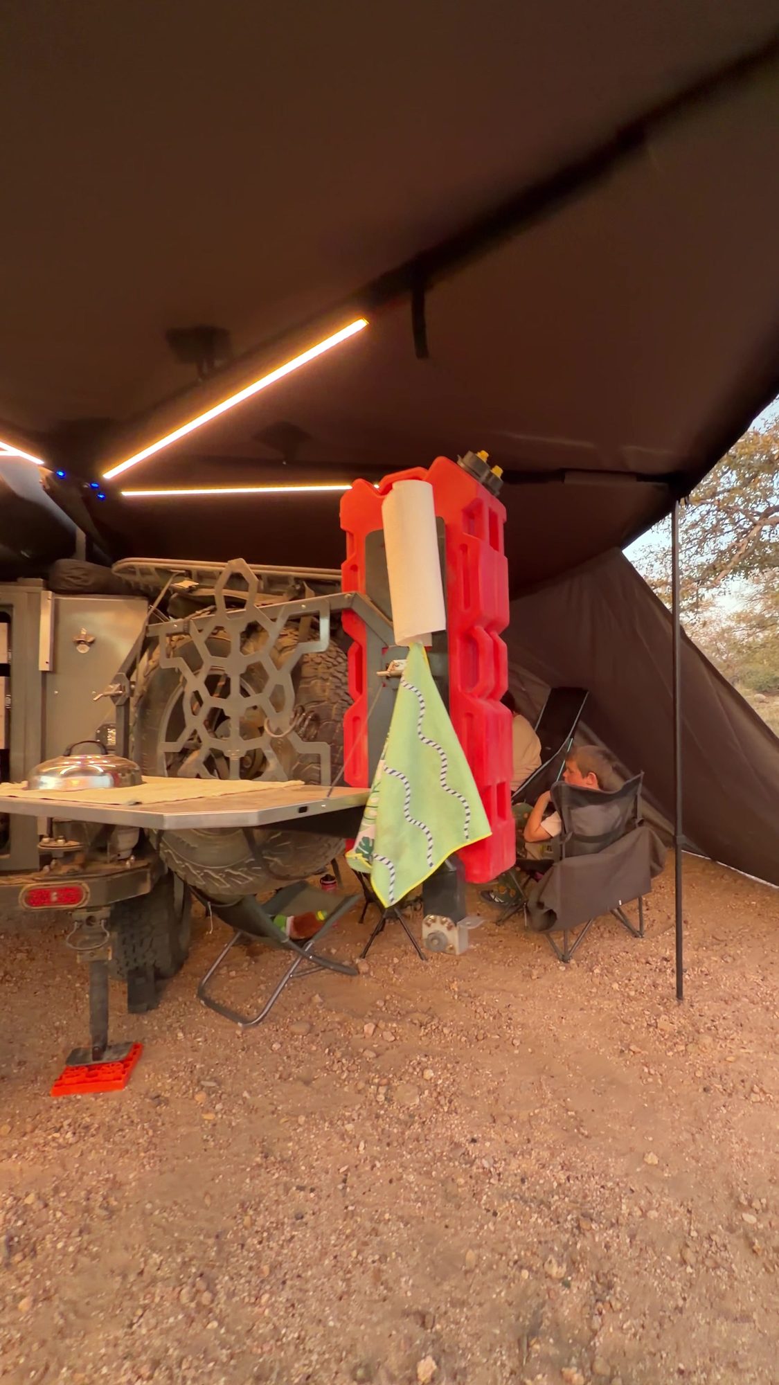 Turtleback trailer kitchen under a lit Taruca awning with a wall panel attached