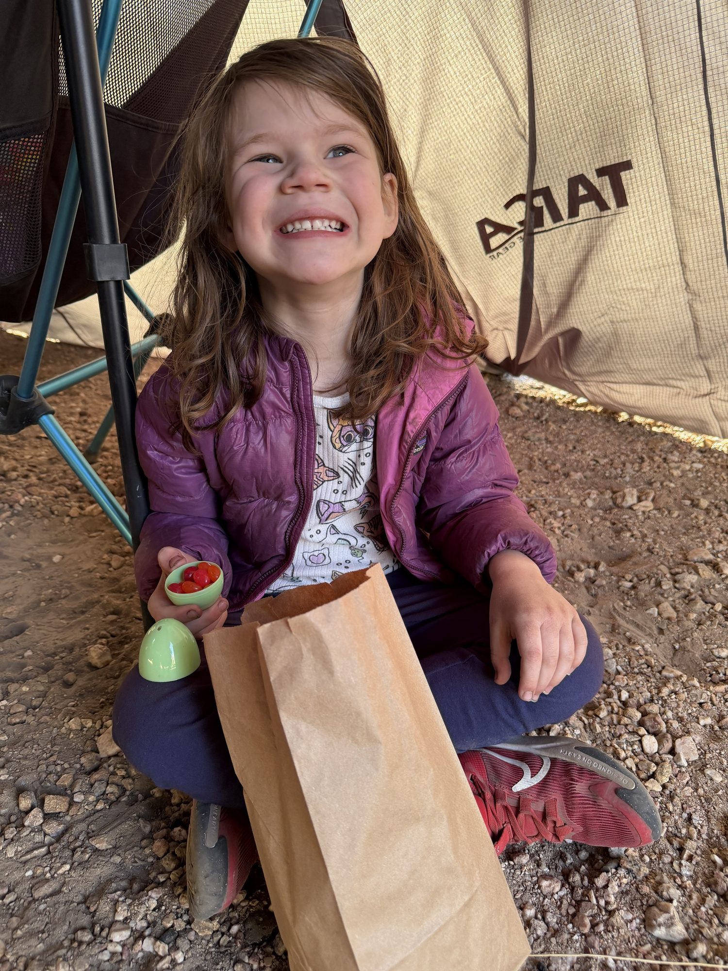 Smiling girl sitting under an awning with a paper bag of Easter treats