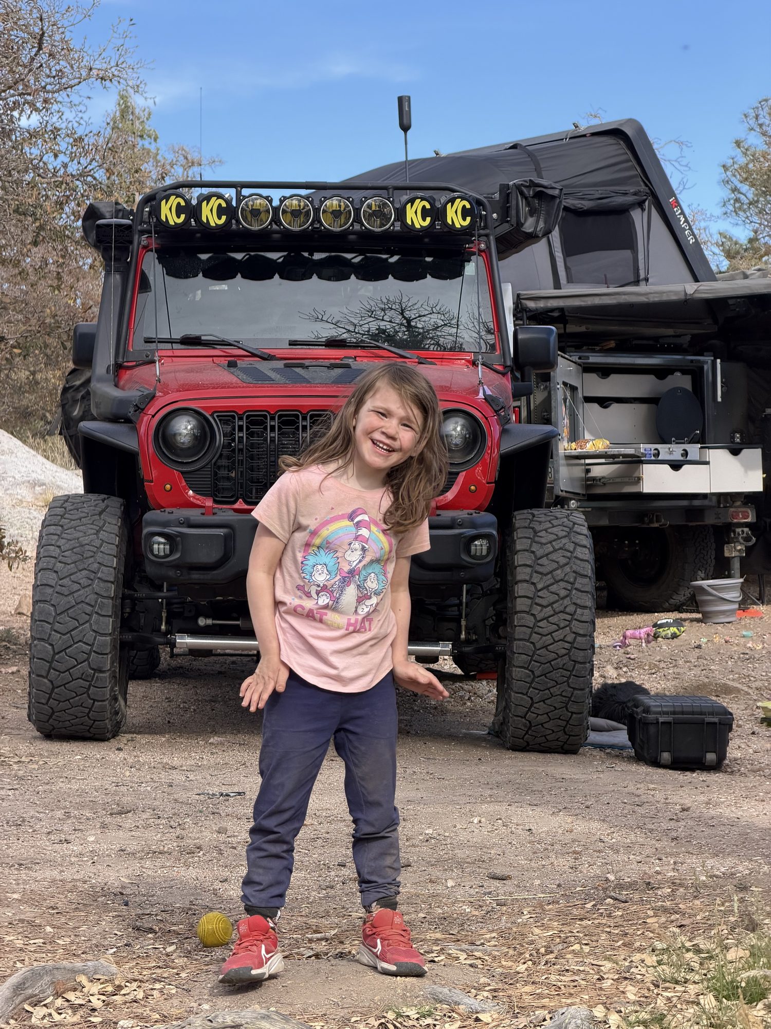 Girl posing in front of a red Jeep and trailer kitchen at camp