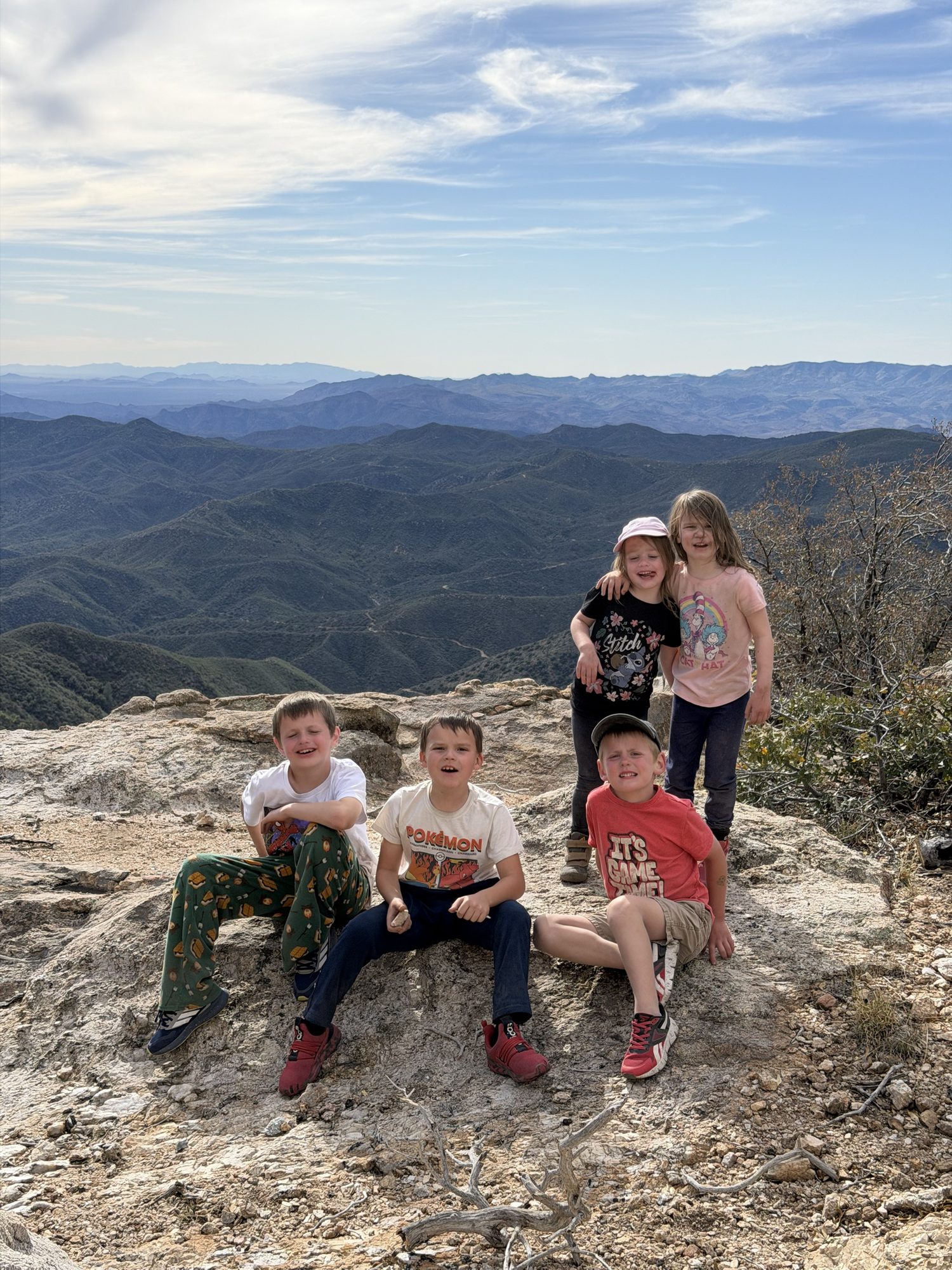 Five kids sitting together on a rocky overlook above a canyon