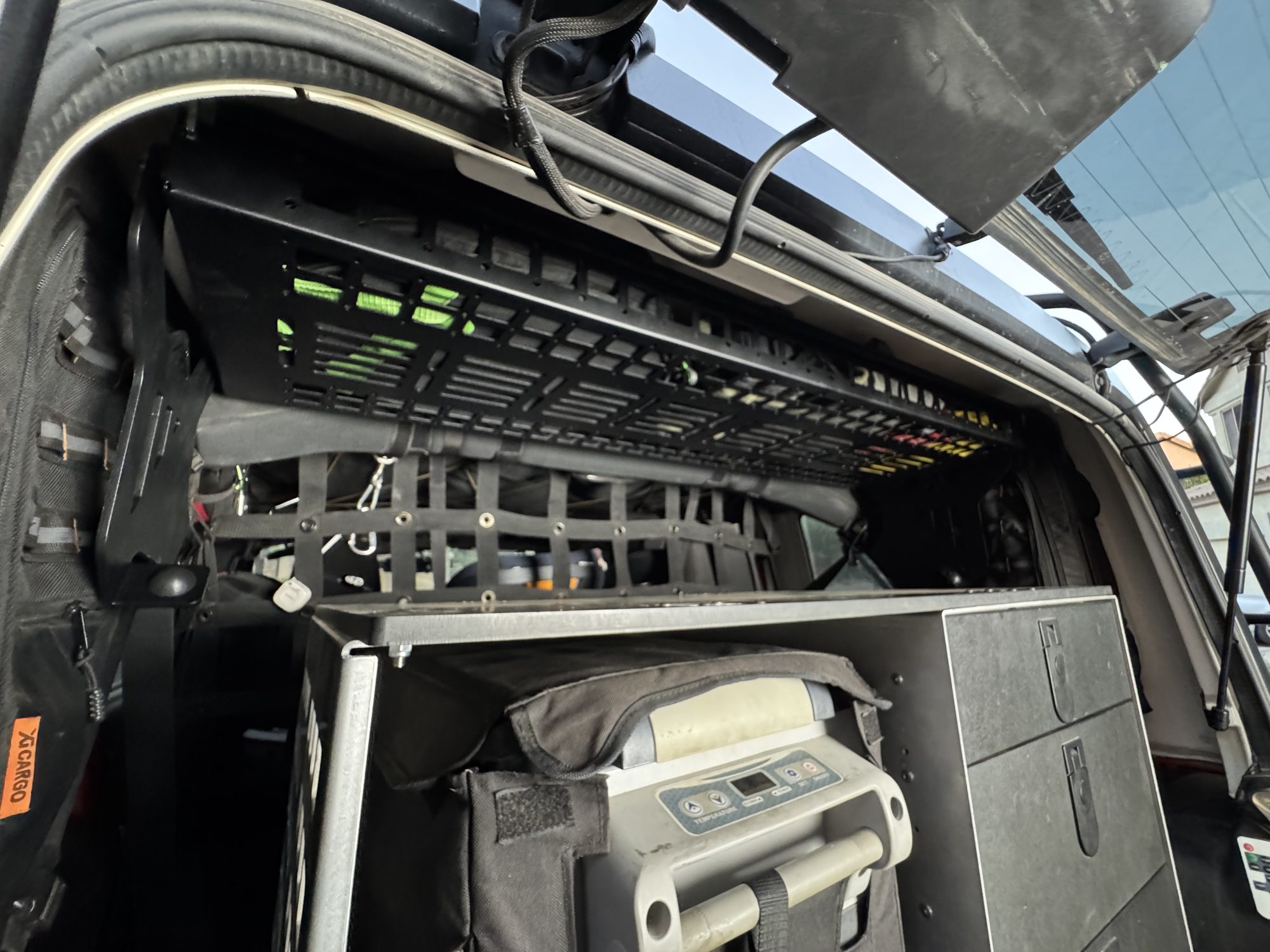 Mountains2Metal attic shelf latched up under the Jeep JKU hardtop showing the MOLLE-slotted underside