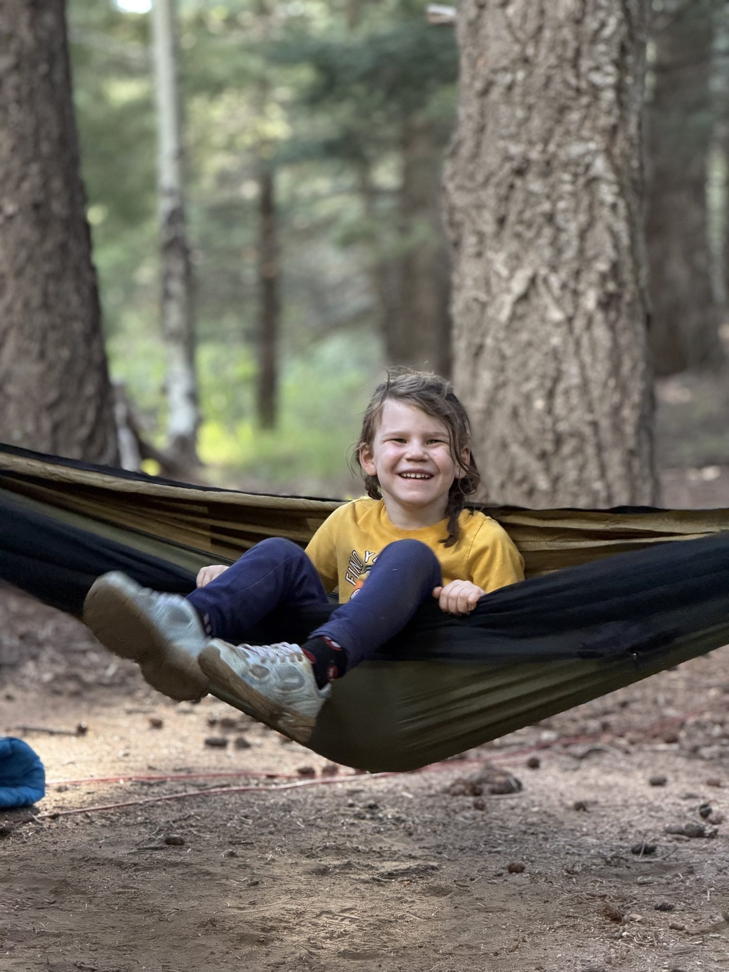 Young girl smiling in a camping hammock among pine trees